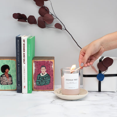 hand lighting a candle with books and a gift behind it