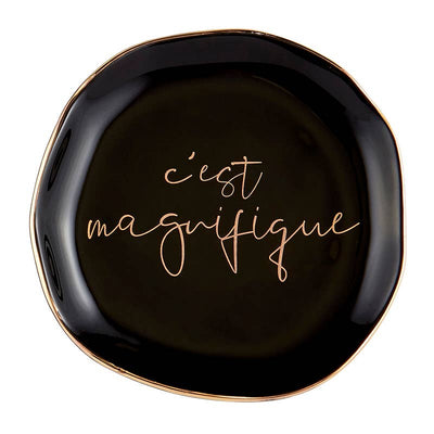 Black circular trinket tray with gold trim and cursive "c'est magnifique" printed in the center