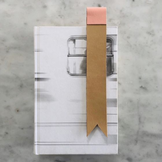 Tan leather bookmark with light pink color trim at top sitting on top of a closed hardcover book