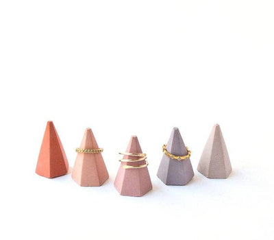 5 tiny hexagonal ring cones in shades of pink laid out with some rings on them