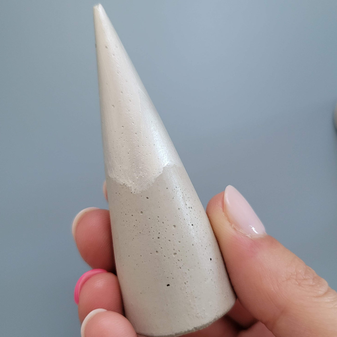 Concrete ring cone dipped in silver paint at the top; held by a hand for scale, ring cone is approximately the length of a finger