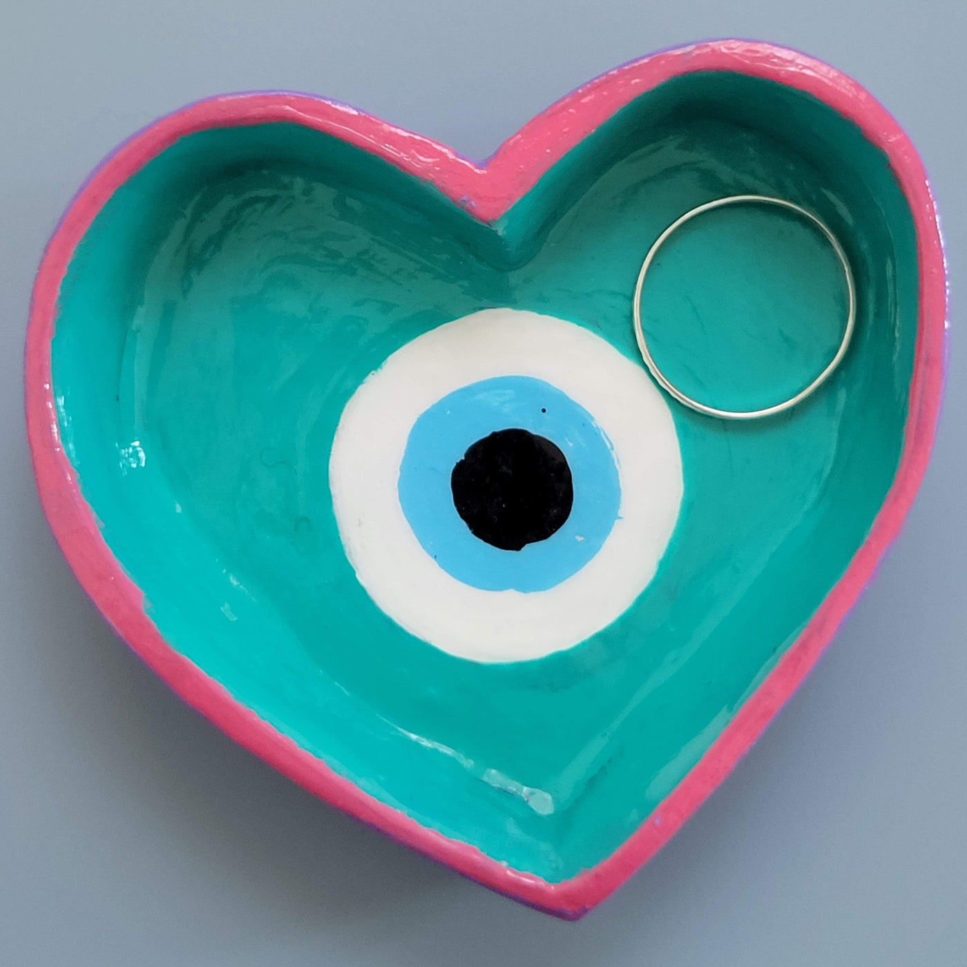 Evil eye painted in a heart shaped ring dish with pink, teal, blue, black and white