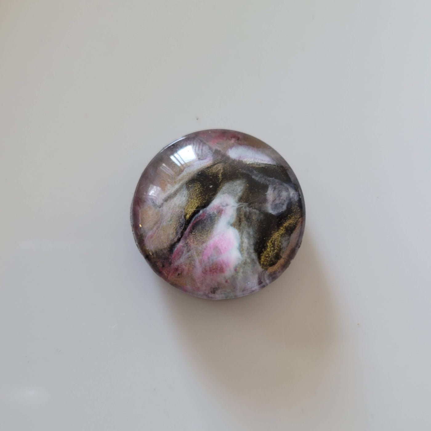 hand-painted circular glass magnet with pink, black, white and gold colors swirled