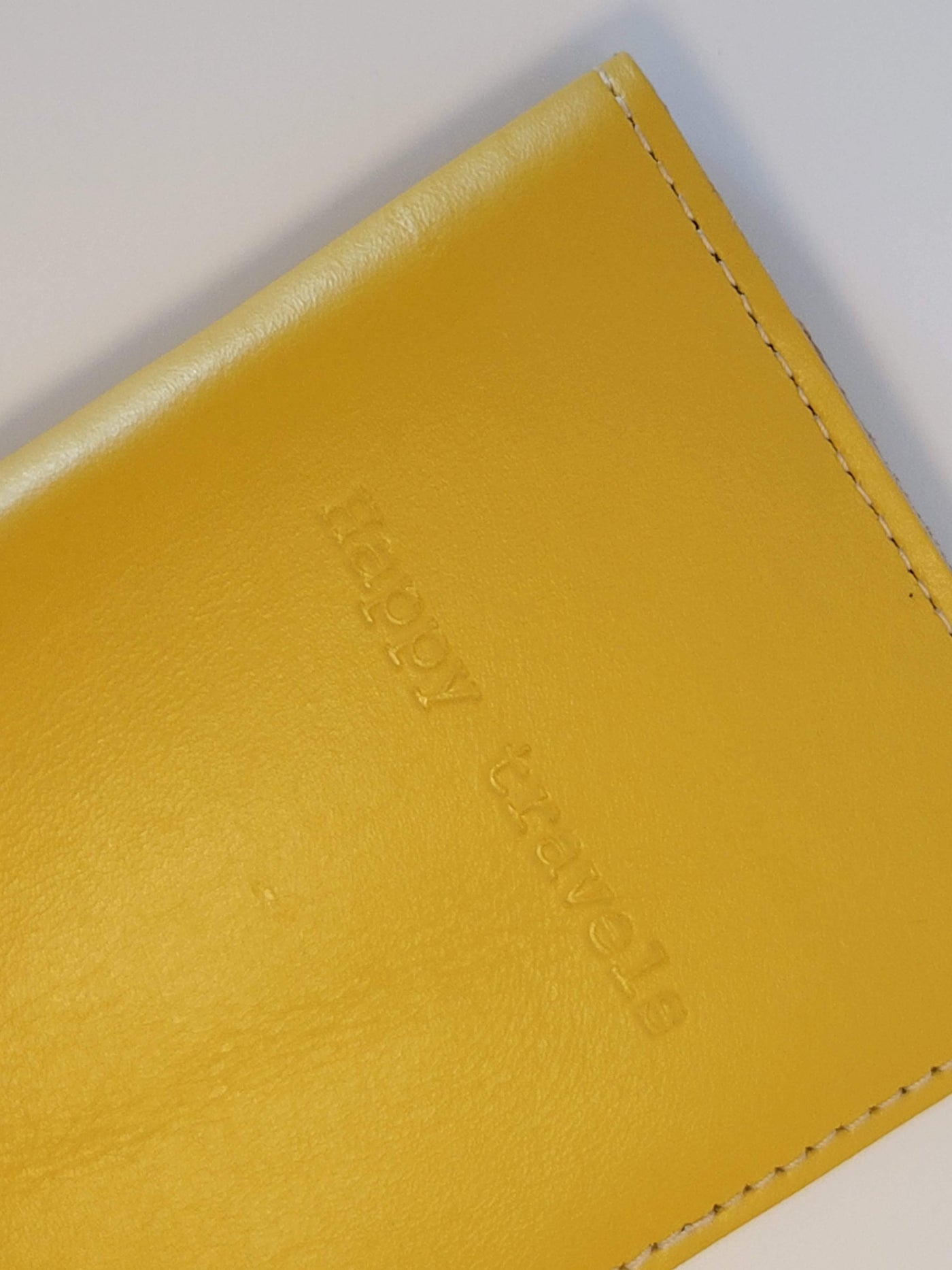 Front close up of mustard yellow passport case with "Happy travels" engraved in the center top of the cover