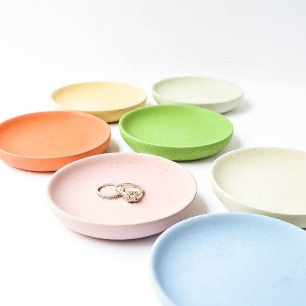 Several round trinket trays in different colors spread out with jewelry sitting in some of them