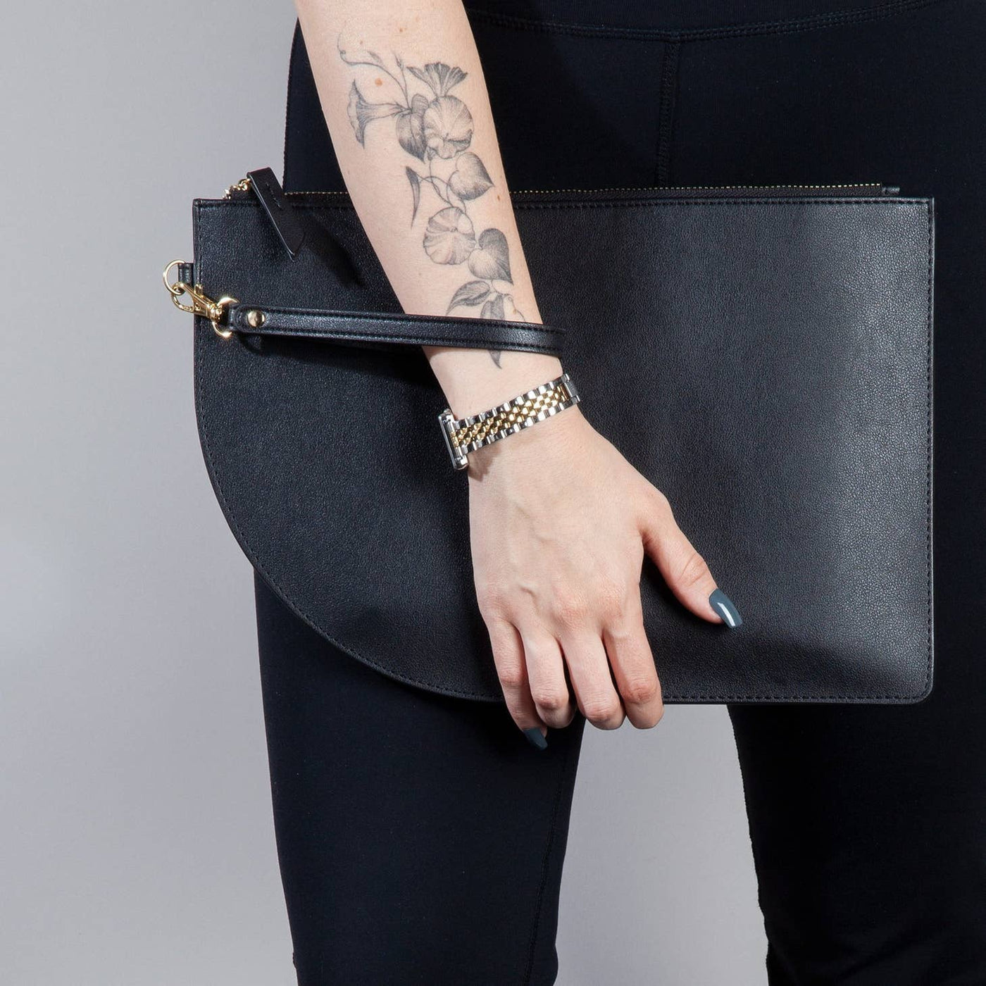 Model holding a black vegan leather flat clutch bag with gold zipper and removable wrist strap