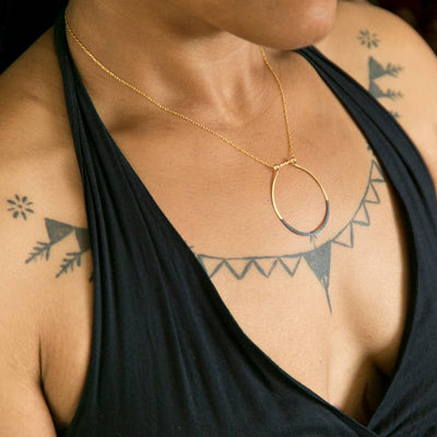 patina dipped brass hand formed pendant on a gold plated chain necklace worn on a model