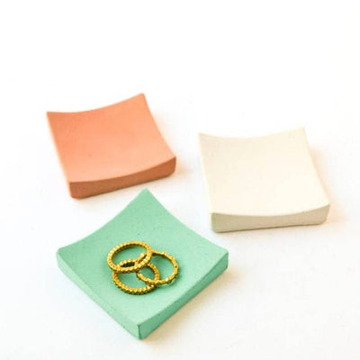 3 tiny square ring dishes in various colors, rings are inside one of them