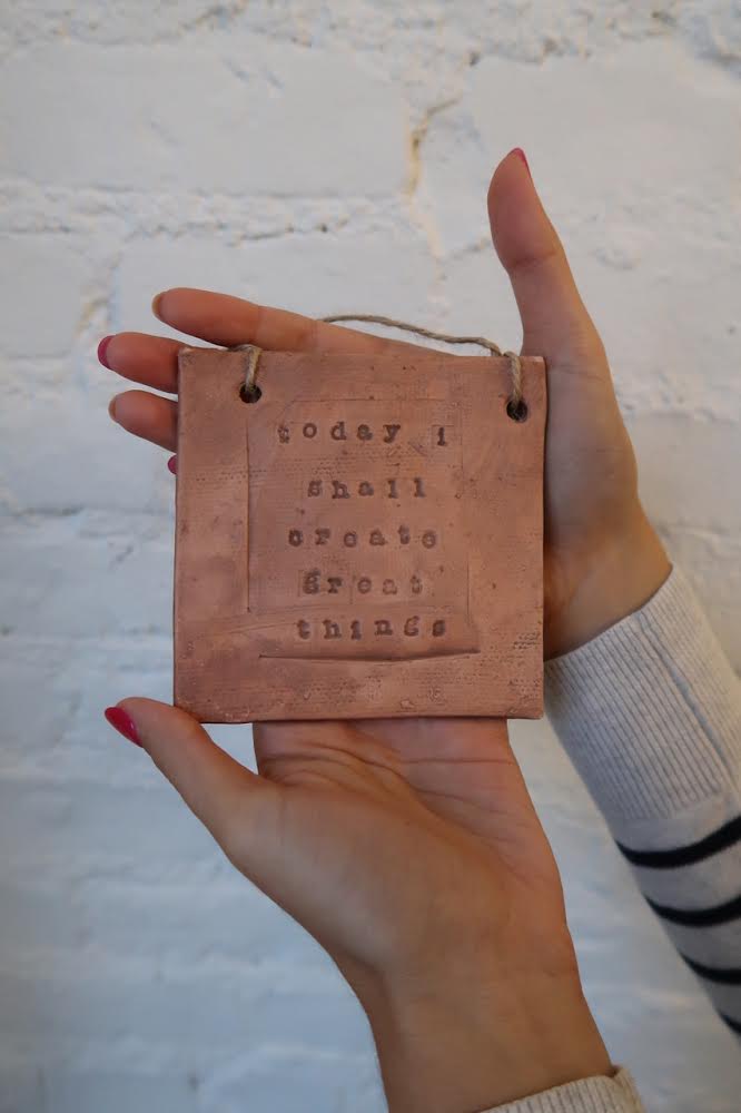unglazed clay tile with inspiring quote being held in hands for scale