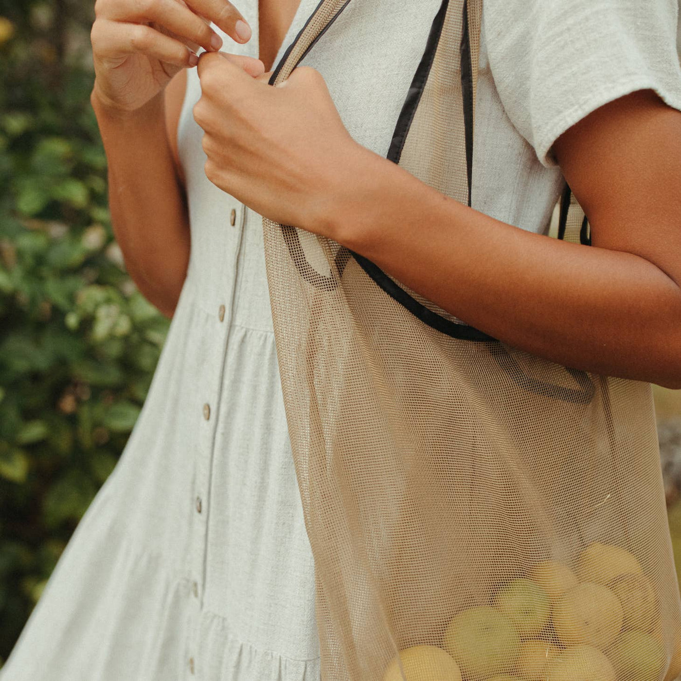close up of mesh farmers market tote bag with model holding it and fruit inside