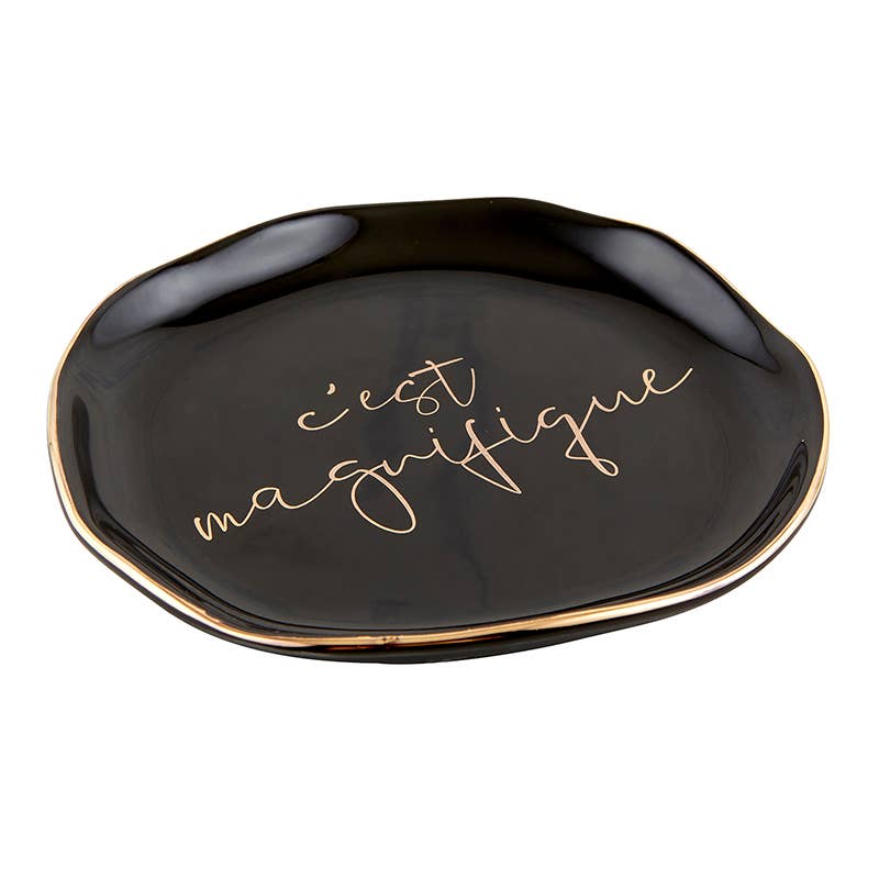 Side view of black circular trinket tray with gold trim and cursive "c'est magnifique" printed in the center