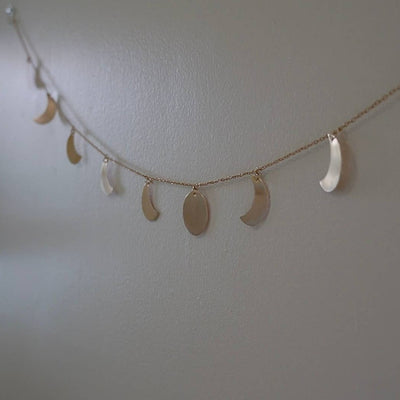 close up of moon phases wall garland with individual moons hand-cut and strung on brass chain