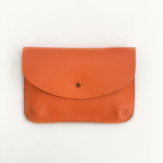 Front of a coral color leather wallet, shaped like an envelope with a metal snap enclosure