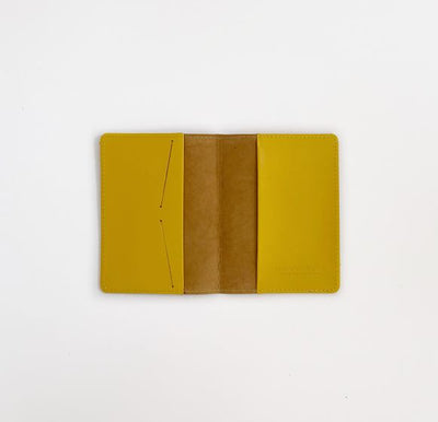 Opened mustard yellow passport case to reveal two pockets, one on each side for passport and other documents, and two slits in one of the pockets for securing ID cards. Interior pockets are also mustard yellow color. 