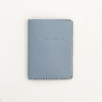 Front of periwinkle passport case with "Happy travels" engraved in the center top of the cover