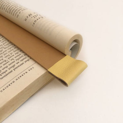 Close up of tan leather bookmark with butter yellow color trim at top in an open book