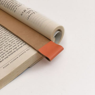 Close up of tan leather bookmark with coral color trim at top in an open book